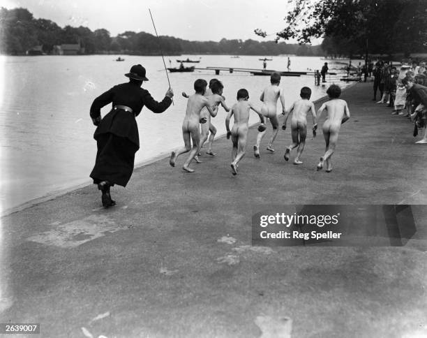 British policewoman chasing after a group of naked street boys by the Serpentine in Hyde Park, London.