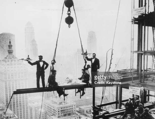 Two waiters serve two steel workers lunch, on a girder high above New York City, 14th November 1930. The building upon which they are perched is the...