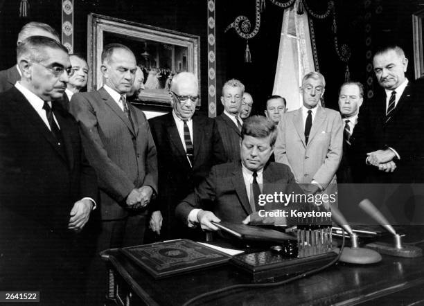 President Kennedy signs the nuclear test ban treaty for the United States watched by a committee of senators, Vice-President Lyndon Baines Johnson...