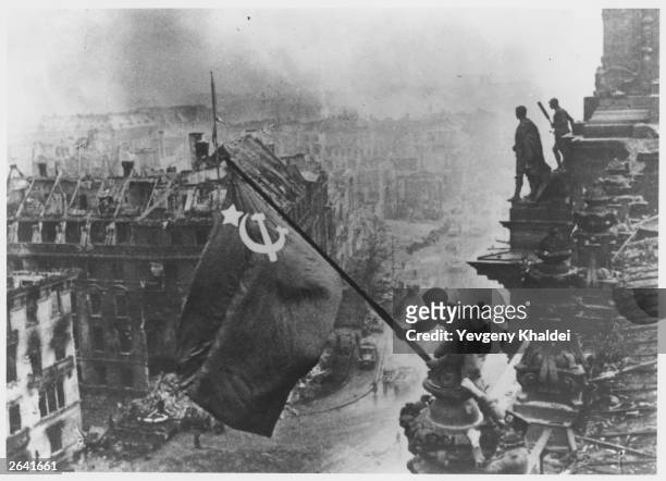 Russian soldiers flying the Red Flag, made from table cloths, over the ruins of the Reichstag in Berlin.