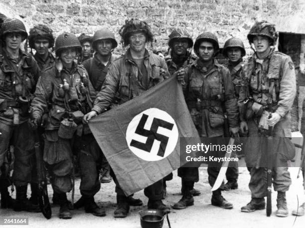 Paratroopers display a Nazi flag captured in an assault on a French village.