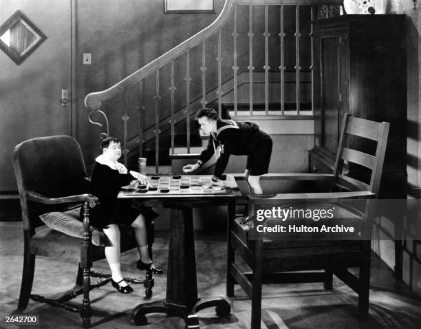 Comedians Stan Laurel and Oliver Hardy , dressed in sailor suits and playing draughts on an oversized set as they appear in the film 'Brats',...