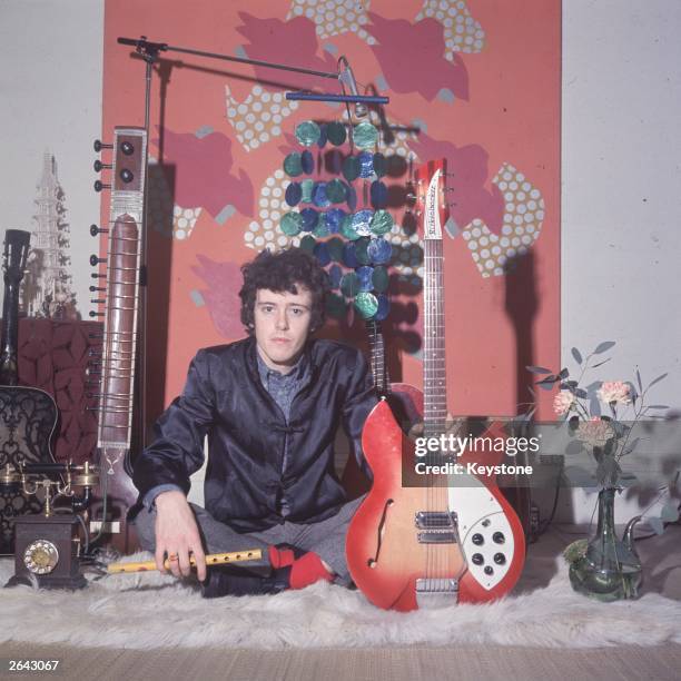 Pop singer Donovan, holding his Rickenbacker guitar and a flute, a sitar and other guitars in the background.