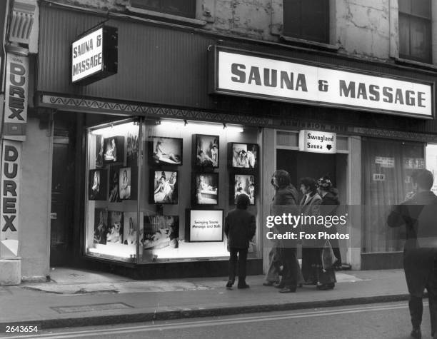 Group of men admire the photographs in the window of Swingland Sauna and Massage Parlour in Soho, London.