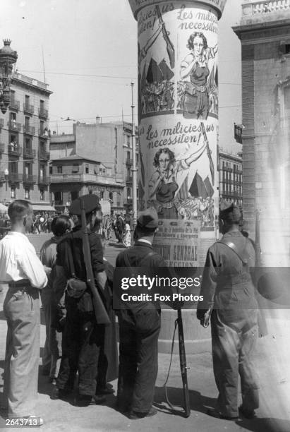 Soldiers read posters in Barcelona calling women to arms during the Spanish Civil War.