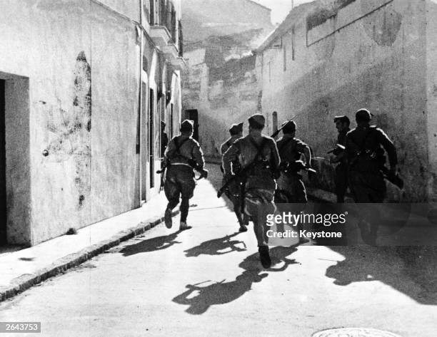 Troops of the Foreign Legion run through the streets of Merida during the Spanish Civil War with their rifles at the ready.