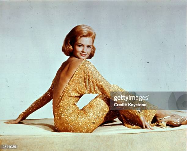 Actress Angie Dickinson wearing a backless gold lame evening dress with batwing sleeves.