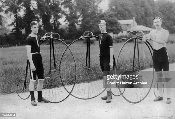 The owners of three penny farthing bicycles stand proudly with their machines.