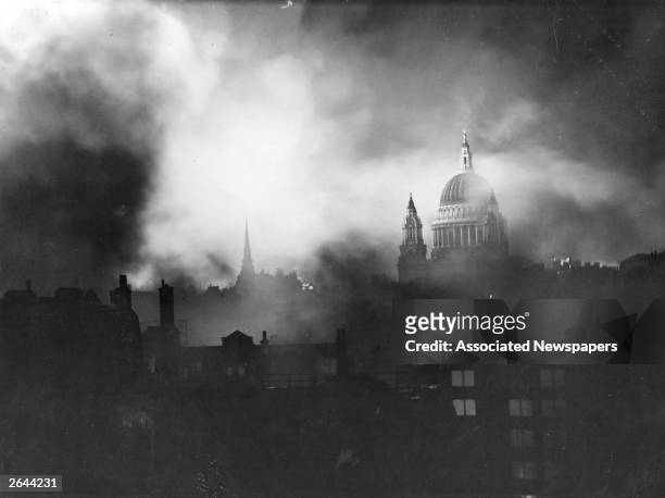 St Paul's Cathedral seen through the flames and smoke of blazing buildings in the City of London during the Blitz.