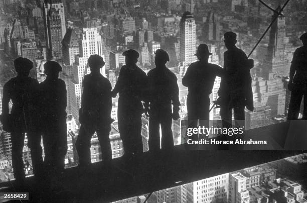 Group of steel workers standing on scaffolding 70 storeys high looking down over New York City from the RCA building.