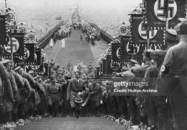 Adolf Hitler, German dictator, ascending the steps at Buckeberg flanked by banner-carrying storm troopers who display the Nazi swastika.