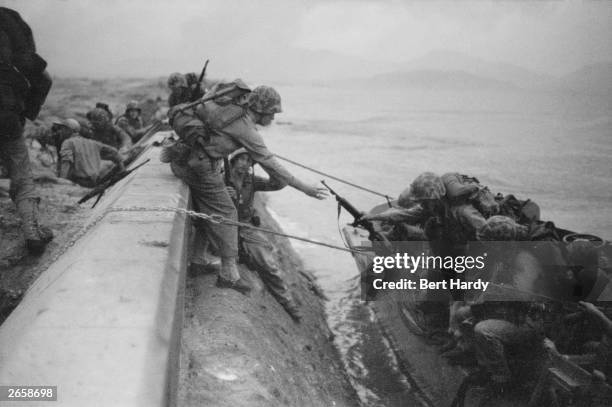 During the Korean War, US Marines land from assault craft and climb over the sea defences at Inchon in South Korea after heavy bombardment of coastal...