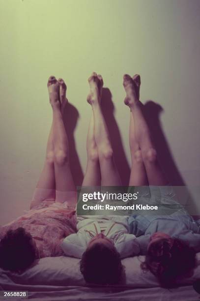 Three women lying with their legs up the wall to show off their coloured nylon stockings. Original Publication: Picture Post - 6694 - It's The Tops -...