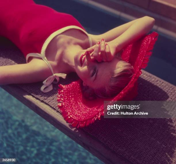 Woman in a red straw hat sunbathing on a diving board.