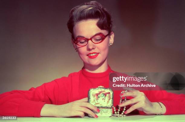 Woman, wearing classic 1950's glasses, looks at the contents of her jewellery box.