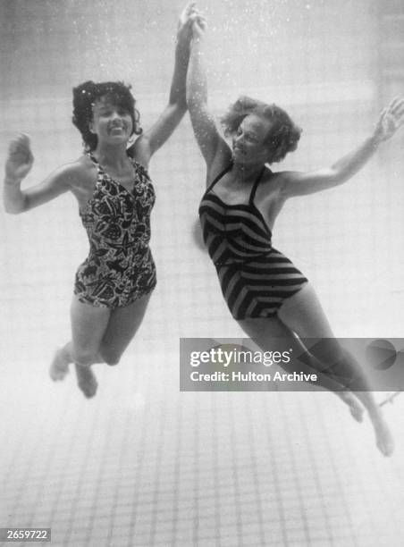 Two models wearing swimming costumes underwater.