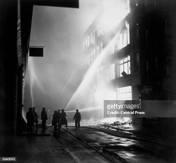 Fire-fighters direct their hoses onto a blazing building after an incendiary raid on the City of London during the Blitz.