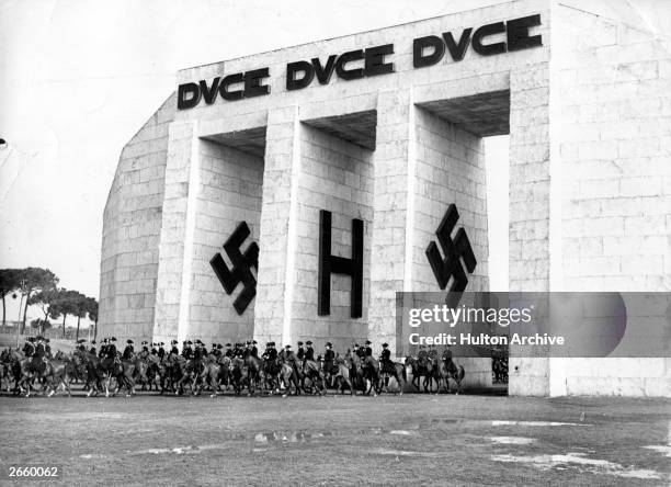 Mounted Carabinieri military police parading through a triumphal arch at Rome to honour the founders of the Axis, Mussolini and Hitler.