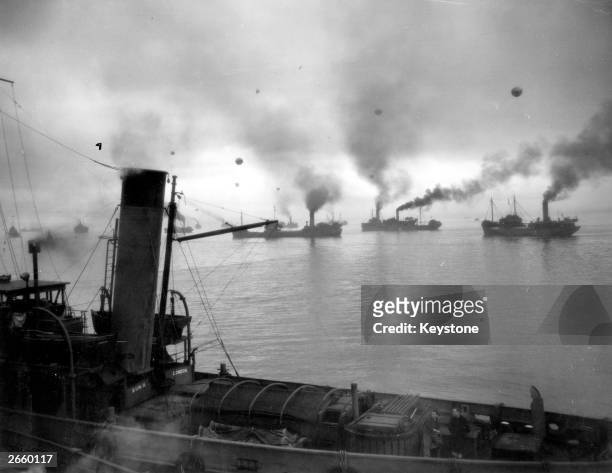 Convoy of coasters sets out at dawn under the protection of escort ships and barrage balloons against air attacks