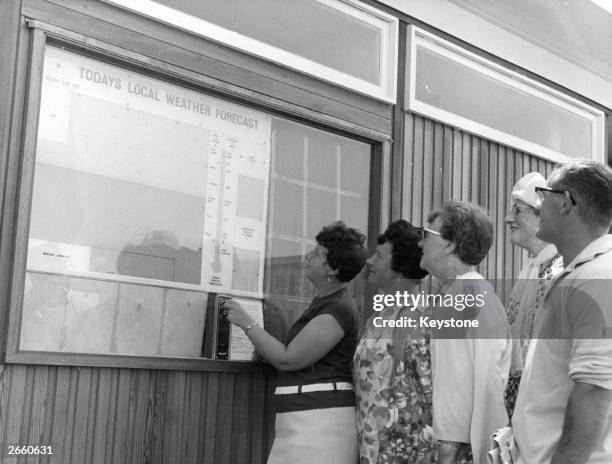 Visitors looking in the penny-in-the-slot forecast board on the sea front at Worthing, Sussex.