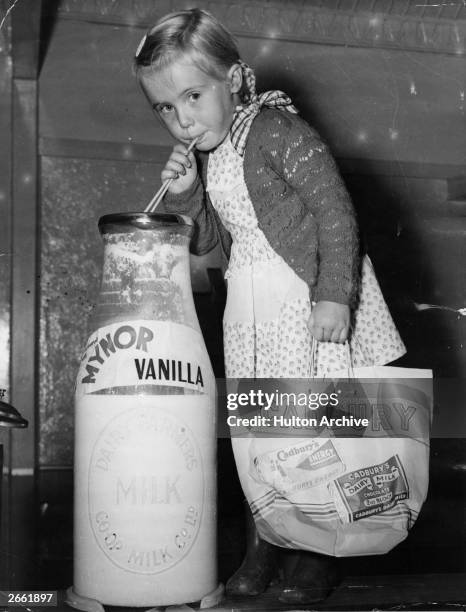 Young girl drinking from an outsize bottle of milk at the 1950 Royal Easter Show in Sydney, carrying a bag advertising Cadbury's chocolate.