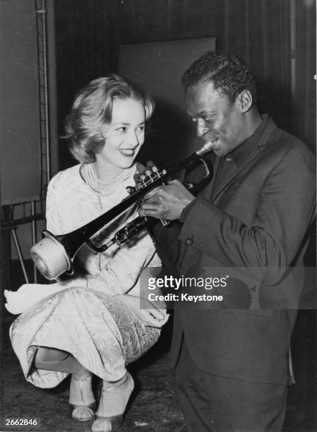 Jazz musician Miles Davis playing his horn, with French actress Jeanne Moreau watching admiringly.