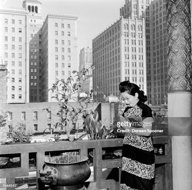 Chinese woman at prayer in front of an incense burner on a balcony outside the main idol room in a temple in Chinatown, San Francisco.