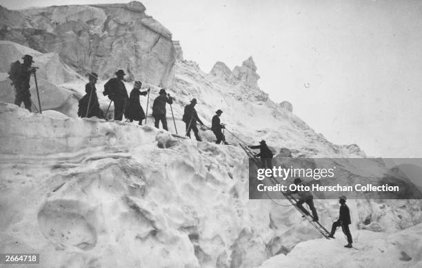 Spanning a crevasse with the help of a ladder, a mixed group go mountaineering in the Alps.