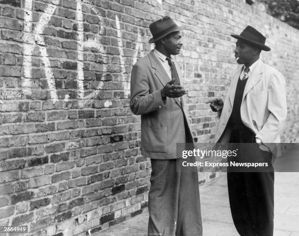 Two Jamaican men talking in a street in Brixton, south London. The graffiti on the wall stands for 'Keep Britain White'.