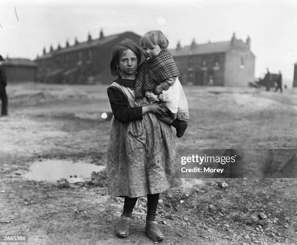 Miner's young daughter carries an even younger child in her arms during a coal strike, Wigan, England, 1921.