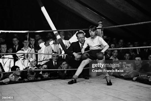 Boxing instructor coaches his young pupil in the Hughes of London boxing pavilion at a Lancashire fair. Original Publication: Picture Post - 2046 -...