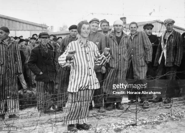 Hungarian Jewish boy in his prison suit of blue and white stripes smiles over the barbed wire at Dachau concentraion Camp. He was expecting to be...