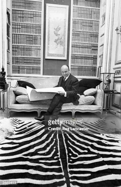 French fashion designer Pierre Balmain looks through a portfolio in his Parisian fashion house. The floor is covered with a luxuriant zebra skin rug.