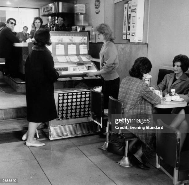 Two women selecting music from a jukebox in a coffee bar.
