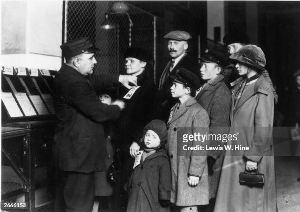 Customs official attaches labels to the coats of a German immigrant family at the Registry Hall on Ellis Island, New York City.