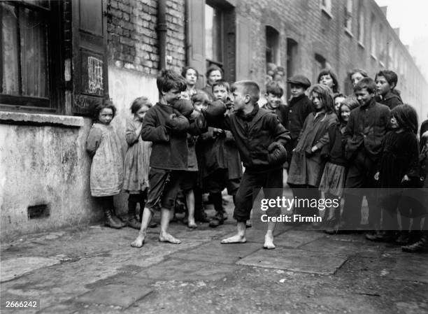 Boys boxing barefoot in a street at Shadwell, London, watched by a crowd of their friends.