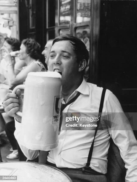 Dressed in shirtsleeves and braces, a drinker in a Paris cafe enjoys an enormous mug of beer.