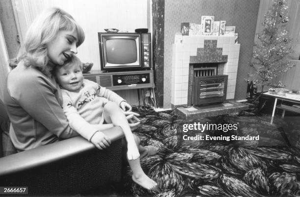 Mrs Carole Ann Smart and child at home in Tooting, south London. There are Christmas cards above the fireplace and an artificial Christmas tree in a...