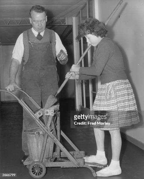 School caretaker, Mr C Haines of Morgans Walk Primary School, Hertford, has patented a mop wringing machine which he is demonstrating to pupil Brenda...