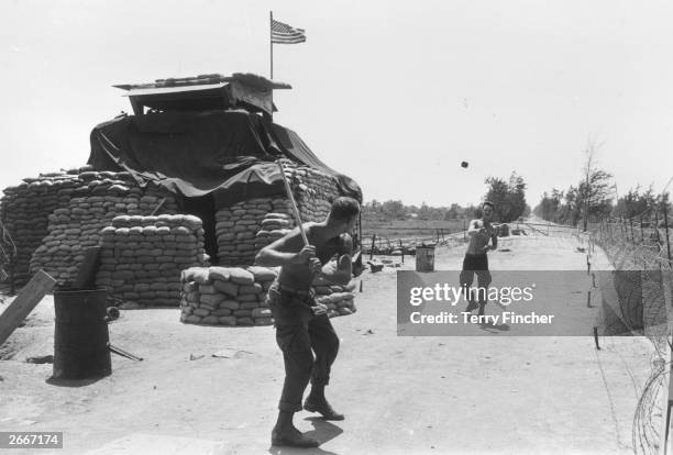 Two US Marines play a makeshift game of baseball, with a trimmed stick as a bat and a ration can as the ball, outside the sandbagged bunker that...