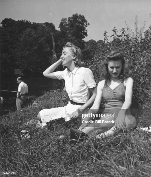 Two women sitting on an English river bank on a sunny day. Original Publication: Picture Post - 822 - A Day On The River - Pub. 1941