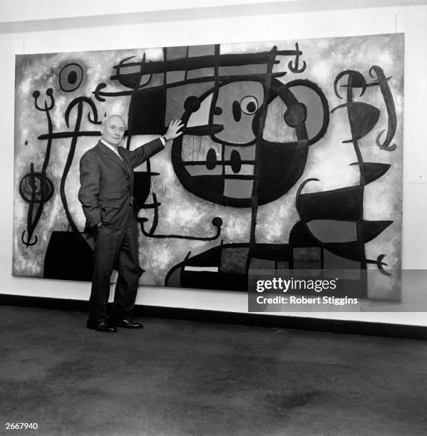 Joan Miro with one of his paintings at his one man exhibition at the Marlborough Fine Art Galleries.