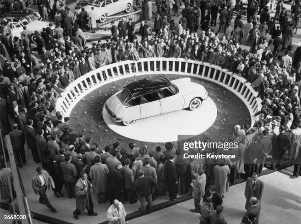 Crowds at the Paris Motor Show in the Grand Palais surround a Citroen DS-19 on display.