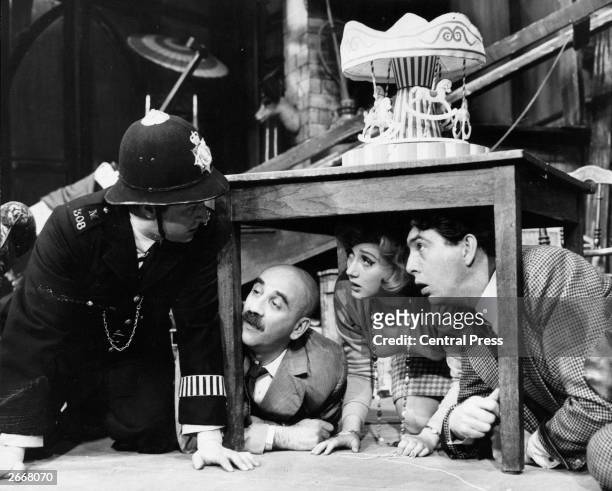 Rehearsal for the comedy 'Everybody Loves Opal' at the Vaudeville Theatre. Robert Arnold as a policeman looks under a table at Warren Mitchell, Liz...