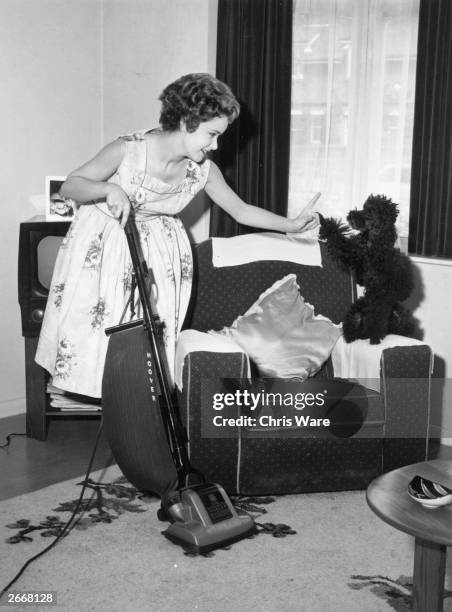 Singer Jill Westlake hoovers her living room in Westgate near Margate, whilst telling off her poodle Bean for interrupting, September 1958.