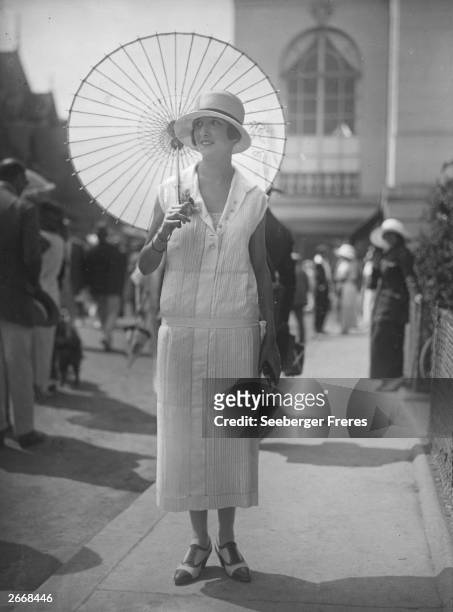 Woman wearing a white pleated drop-waist dress, carrying a parasol, near the casino in Deauville, France.