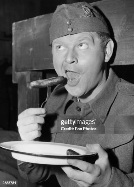 English comedian Benny Hill eating a sausage in Home Guard uniform.