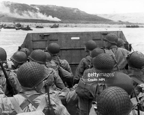 American assault troops in a landing craft near a beachhead in northern France. The landing is supported by naval gunfire.