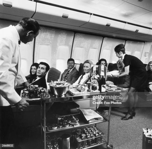 Steward and stewardess serving first-class passengers with drinks and refreshments on board a Boeing 747.