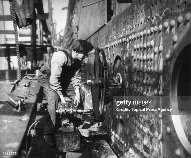 Workman using pneumatically-powered equipment to cut sidelights in the hull of the Cunard liner Aquitania at the John Brown & Co shipyard on...